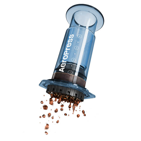 Aeropress coffee maker with coffee grounds spilling out on a white background