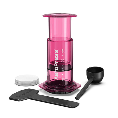 Pink Aeropress coffee maker with black components on a white background