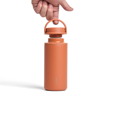 Ceramic water bottle with a hand holding the lid on a white background