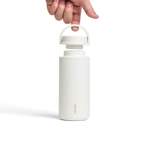 White insulated bottle with a hand holding the lid on a white background
