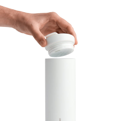 Hand holding a white bottle cap above a white bottle on a white background