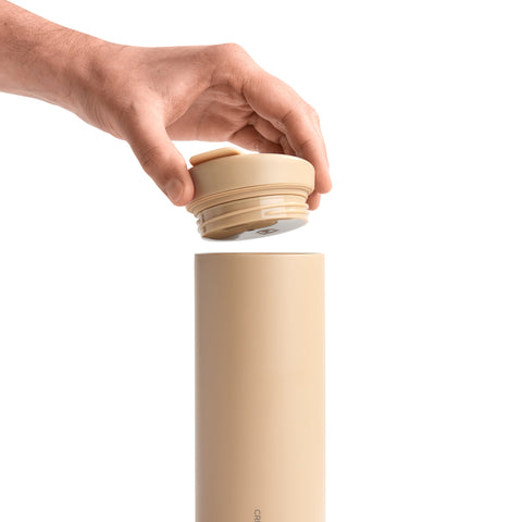 Beige thermos bottle with a hand opening the lid on a white background