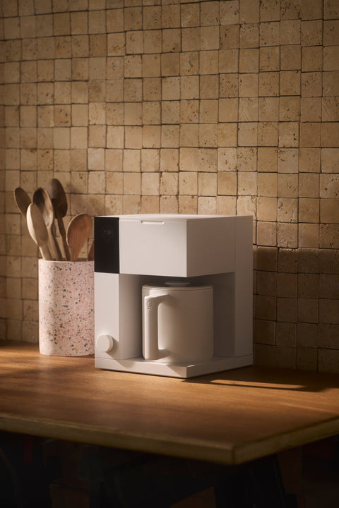 White Fellow Aiden coffee maker on a wooden countertop with a tiled wall background