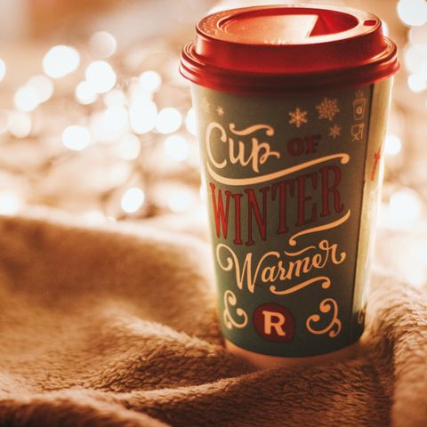 Coffee cup with 'Cup of Winter Warmer' text on a soft fabric background