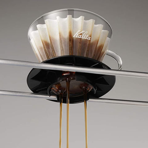 Coffee dripper with Kalita Wave 185 Glass Dripper and coffee dripping into a black container on a gray background.
