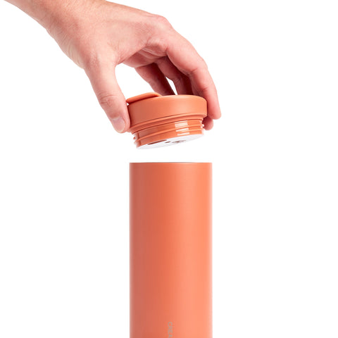 Hand placing a terracotta-colored lid on a cylindrical container against a white background
