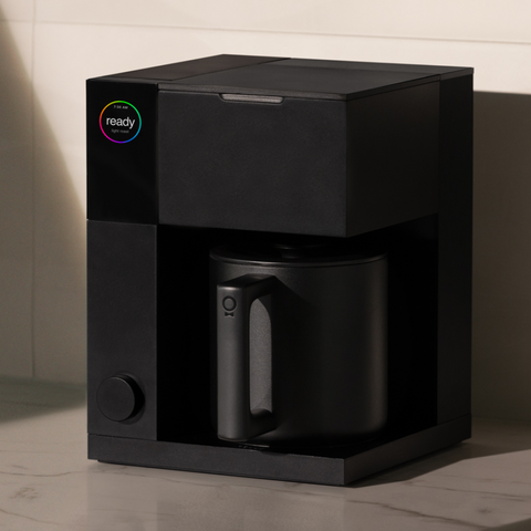 Fellow Aiden  Black coffee maker with a mug on a neutral background