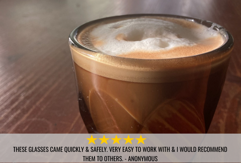 Glass of coffee with a thick layer of foam on a wooden surface, featuring a five-star rating and anonymous review text.