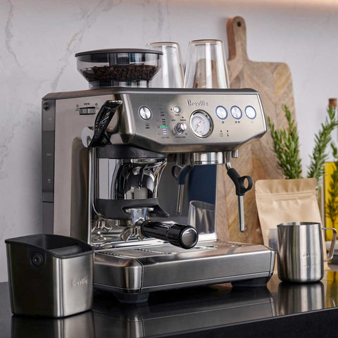 Breville espresso machine on a kitchen counter with ingredients and tools.