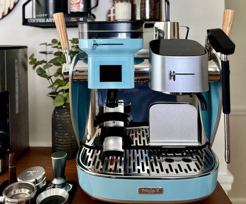 Blue and silver La Seine X espresso machine on a wooden surface with coffee-making accessories.