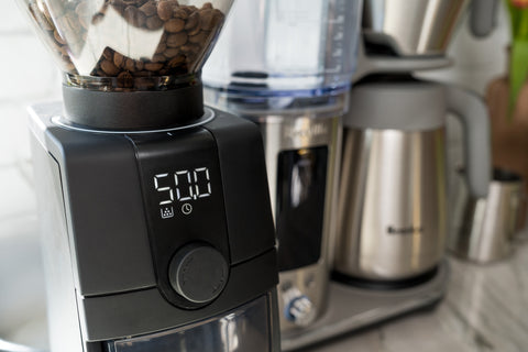 Blender with coffee beans and a kettle in the background on a kitchen counter.