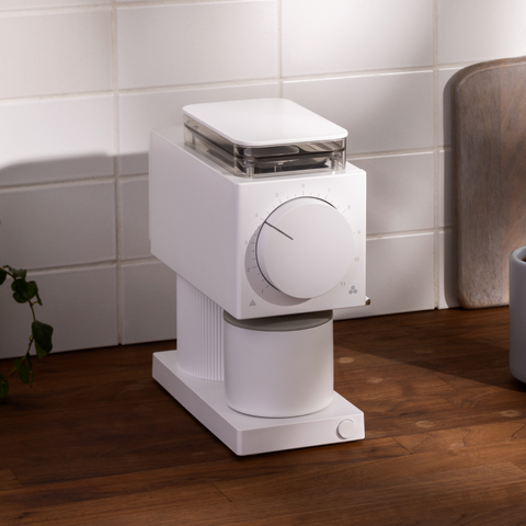 White coffee grinder on a wooden floor with a tiled wall background