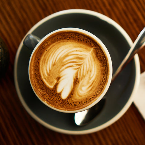 Cappuccino with latte art on a saucer with a spoon on a wooden table