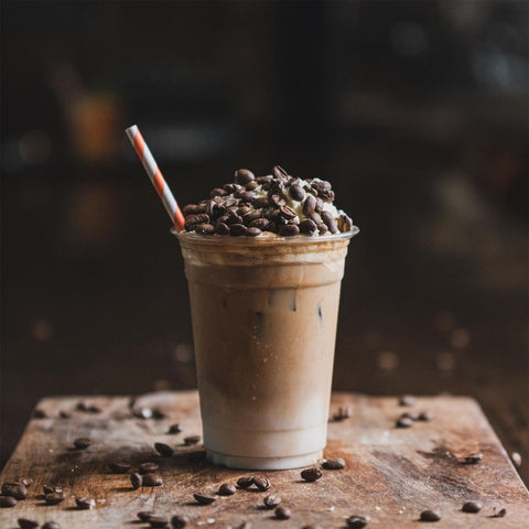 Iced coffee with coffee beans on top in a clear cup on a wooden surface.