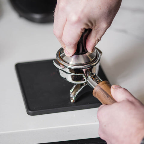 Person using a coffee tamper on a coffee grinder