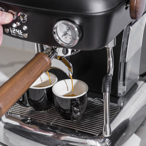 Ascaso Dream PID Automatic Home Espresso Machine - Anthracite dispensing coffee into two cups with a person's hand adjusting the machine.
