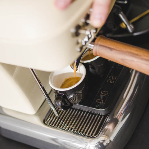 Espresso being poured from a machine into a cup held by a hand.