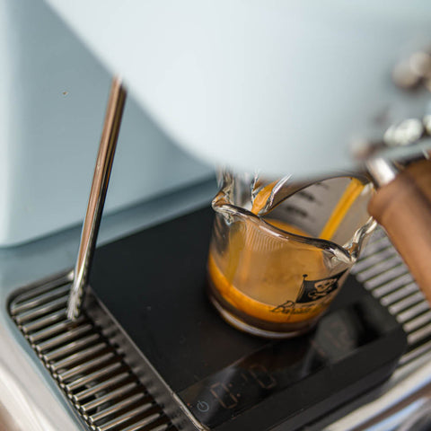 Espresso being poured into a glass measuring cup from an Ascaso Dream PID Automatic Home Espresso Machine - Kid Blue 