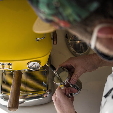 Person using a Ascaso Dream PID Automatic Home Espresso Machine - Sun Yellow  with a close-up of hands holding a scoop and container.