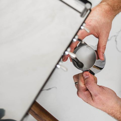 A person frothing milk on a Ascaso Steel DUO PID Espresso Machine (White)