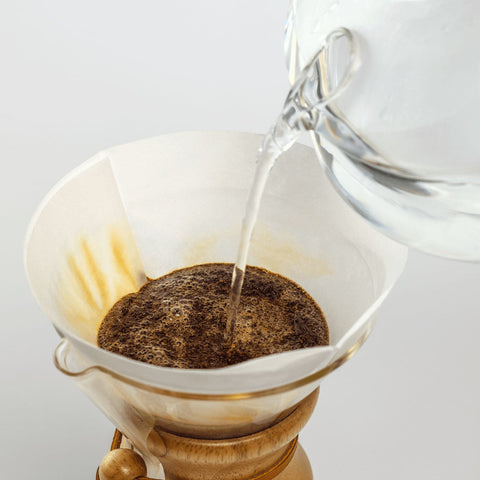 Pouring water into a chemex coffee filter with ground coffee on a white background