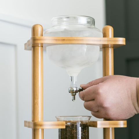 Hand using a wooden and glass coffee brewing device on a plain background