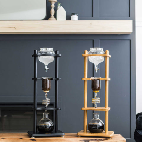 Two coffee brewing apparatuses, one black and one wooden, on a kitchen counter.