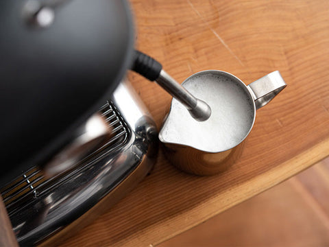 Ascaso Dream PID Automatic Home Espresso Machine - Anthracite with a milk frothing pitcher on a wooden surface