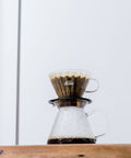 Coffee brewing device with Kalita Wave 185 Glass Dripper  on a wooden surface and light gray background