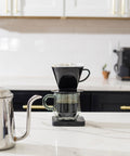 Coffee brewing setup on a kitchen counter with a glass carafe and black Kalita Plastic coffee filter.
