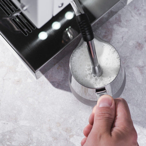 Foamy milk being extracted from a coffee machine into a metal pitcher.