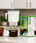 Toddy cold brew system on a kitchen counter with a glass of iced coffee.
