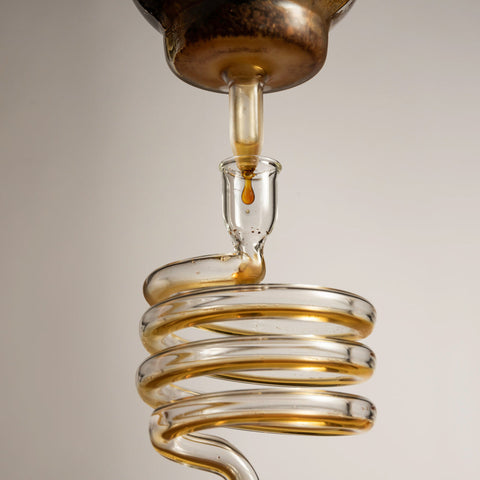 Close-up of a coiled glass object with a liquid being dripped into it against a neutral background