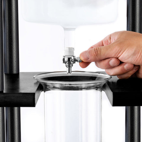Hand using a  Yama 25 Cup Cold Brew Tower  with a clear glass container on a white background