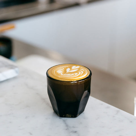 Espresso shot with latte art in a dark glass cup on a marble counter.