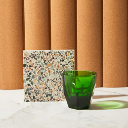 Green glass cup and terrazzo coaster on a marble surface with a brown curtain background