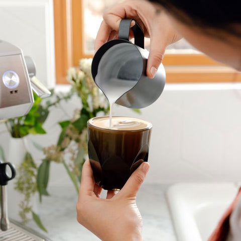 Person pouring steamed milk into a coffee cup with a blurred background
