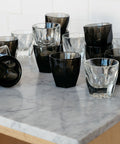 Collection of black and clear glass tumblers on a marble countertop.