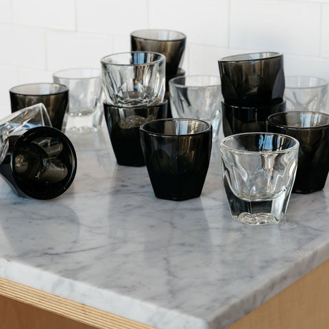 Collection of black and clear glass tumblers on a marble countertop.
