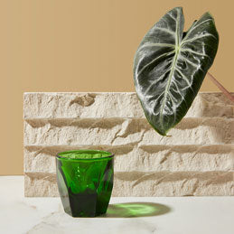 Green glass vase on a light surface with a beige wall and stone block in the background