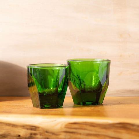 Two green glass tumblers on a wooden surface with a beige background